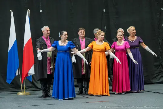 Grupa tancerzy w kolorowych strojach balowych na scenie.
