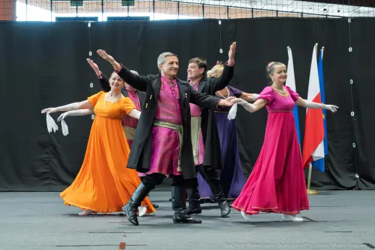 Grupa tancerzy w kolorowych strojach wykonuje układ taneczny na scenie.