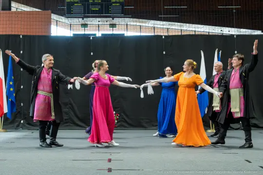 Grupa tancerzy w kolorowych strojach wykonuje układ taneczny na scenie.