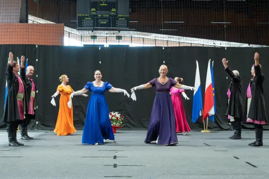 Grupa tancerzy w kolorowych strojach wykonuje taniec na scenie.