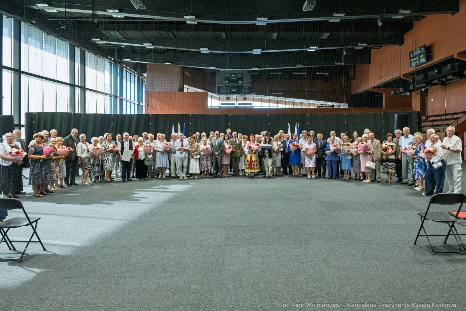 Grupa seniorów trzymających kwiaty w sali.  Autor: Piotr Wojnarowski