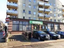 Centrum rehabilitacyjne z parkingiem i budynkiem mieszkalnym w tle.