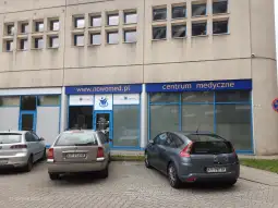 Centrum medyczne Nowomed z widocznymi samochodami zaparkowanymi przed budynkiem.