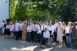 Grupa uczniów w białych koszulach i ich nauczycieli na zewnątrz, w tle zieleń drzew.
