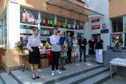 Uroczystość z przemówieniami i dekoracjami, uczestnicy stoją przed budynkiem.
