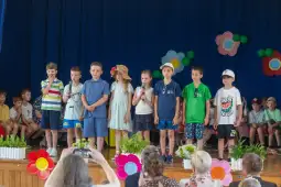 Grupa dzieci na scenie podczas występu, trzymają mikrofony, w tle widownia.