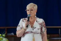 Kobieta z mikrofonem w eleganckiej sukience, wygłaszająca przemówienie.