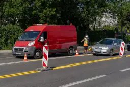 Ruch drogowy z kontrolą, czerwony furgon i samochód osobowy przy barierkach.