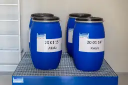 Niebezpieczne substancje chemiczne w niebieskich beczkach z etykietami.