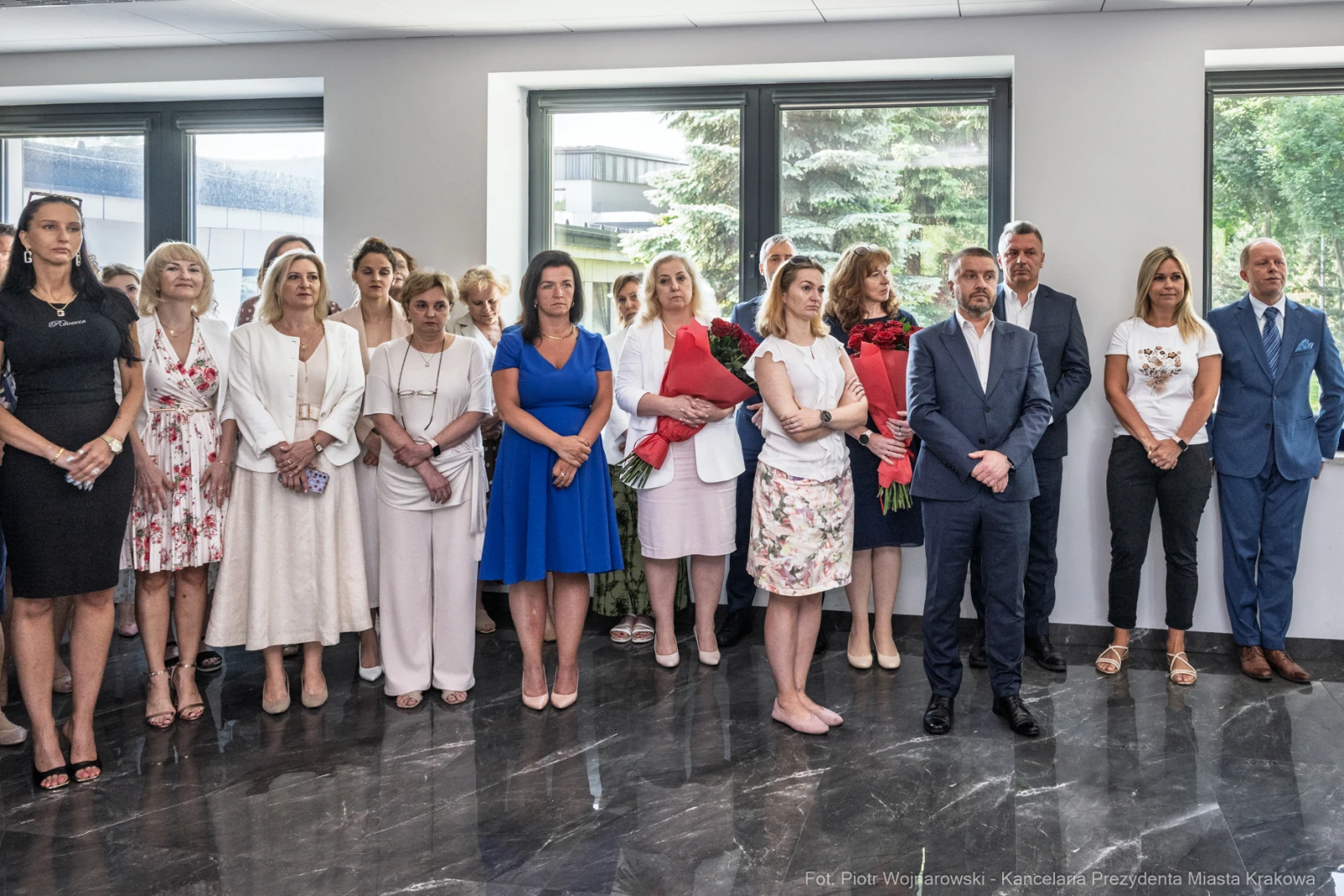 Grupa osób w eleganckich strojach, stojących w sali, niektórzy trzymają kwiaty.  Autor: Piotr Wojnarowski