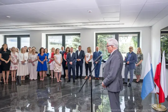 Spotkanie grupy ludzi w eleganckim wnętrzu, mężczyzna przemawia do zebranych.