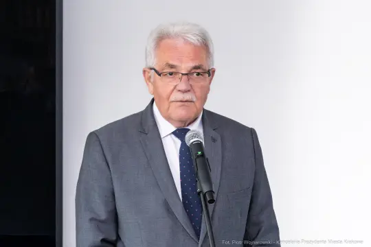 Mężczyzna w szarym garniturze przemawia do mikrofonu.