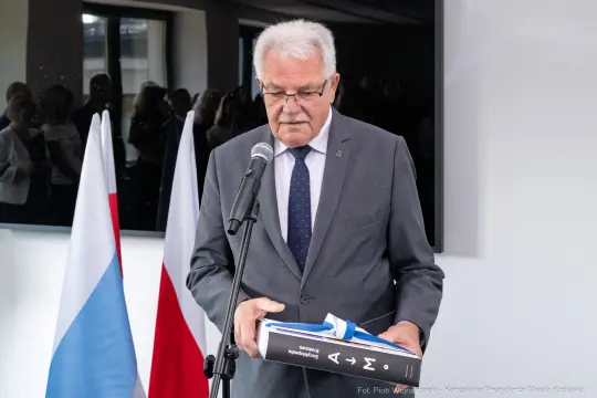Mężczyzna z mikrofonem trzyma teczkę, w tle flagi Polski i Rosji.