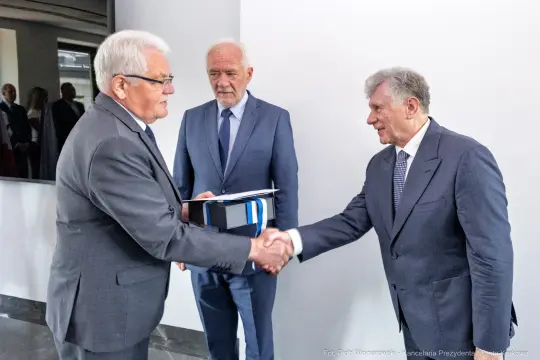 Trzech mężczyzn w garniturach, uścisk dłoni, formalne spotkanie.