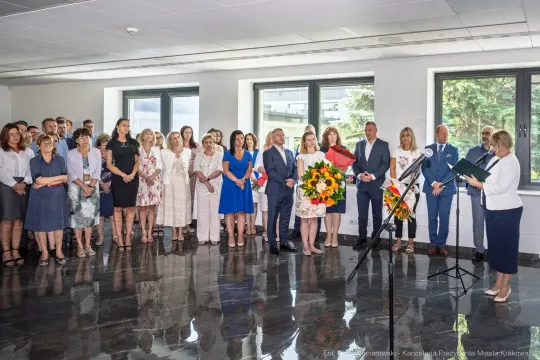 Uroczystość z kwiatami, przemówienia i zgromadzeni goście w eleganckim wnętrzu.