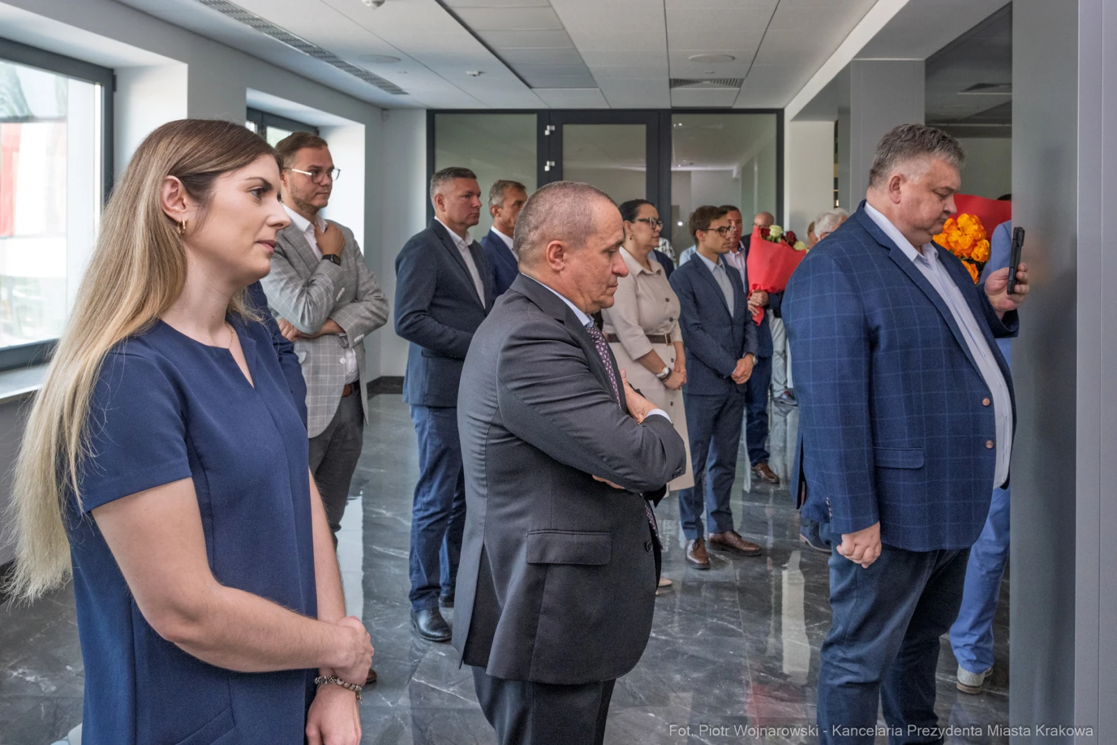 Grupa osób w eleganckich strojach, słuchających przemówienia w nowoczesnym wnętrzu.  Autor: Piotr Wojnarowski