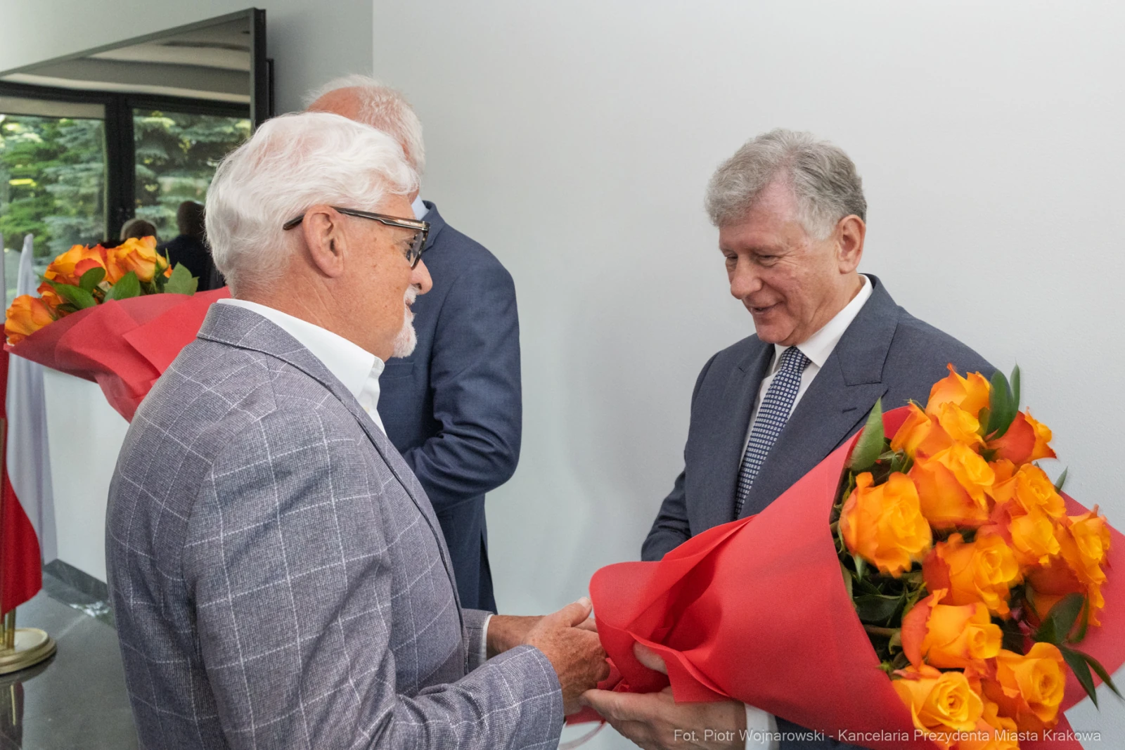Dwaj mężczyźni wymieniają się kwiatami, w tle flagi Polski.  Autor: Piotr Wojnarowski