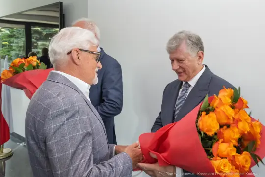 Dwaj mężczyźni wymieniają się kwiatami, w tle flagi Polski.