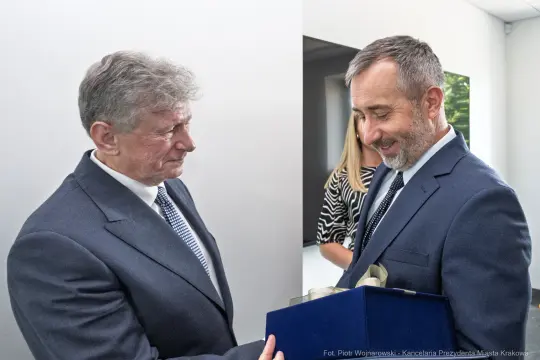 Dwaj mężczyźni wymieniają się prezentem w formalnej atmosferze.