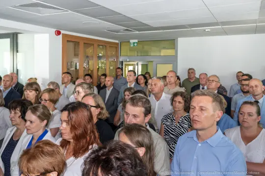 Grupa ludzi w sali, uczestniczących w spotkaniu lub konferencji.