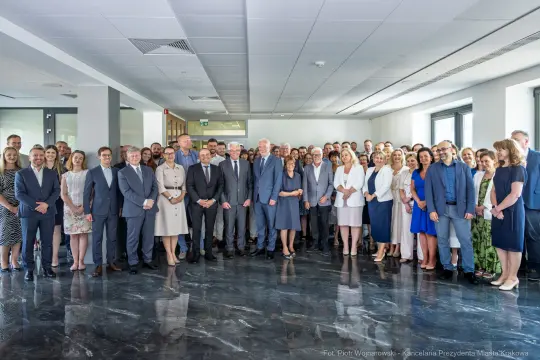 Grupa ludzi w formalnych strojach, stojących razem w nowoczesnym wnętrzu.