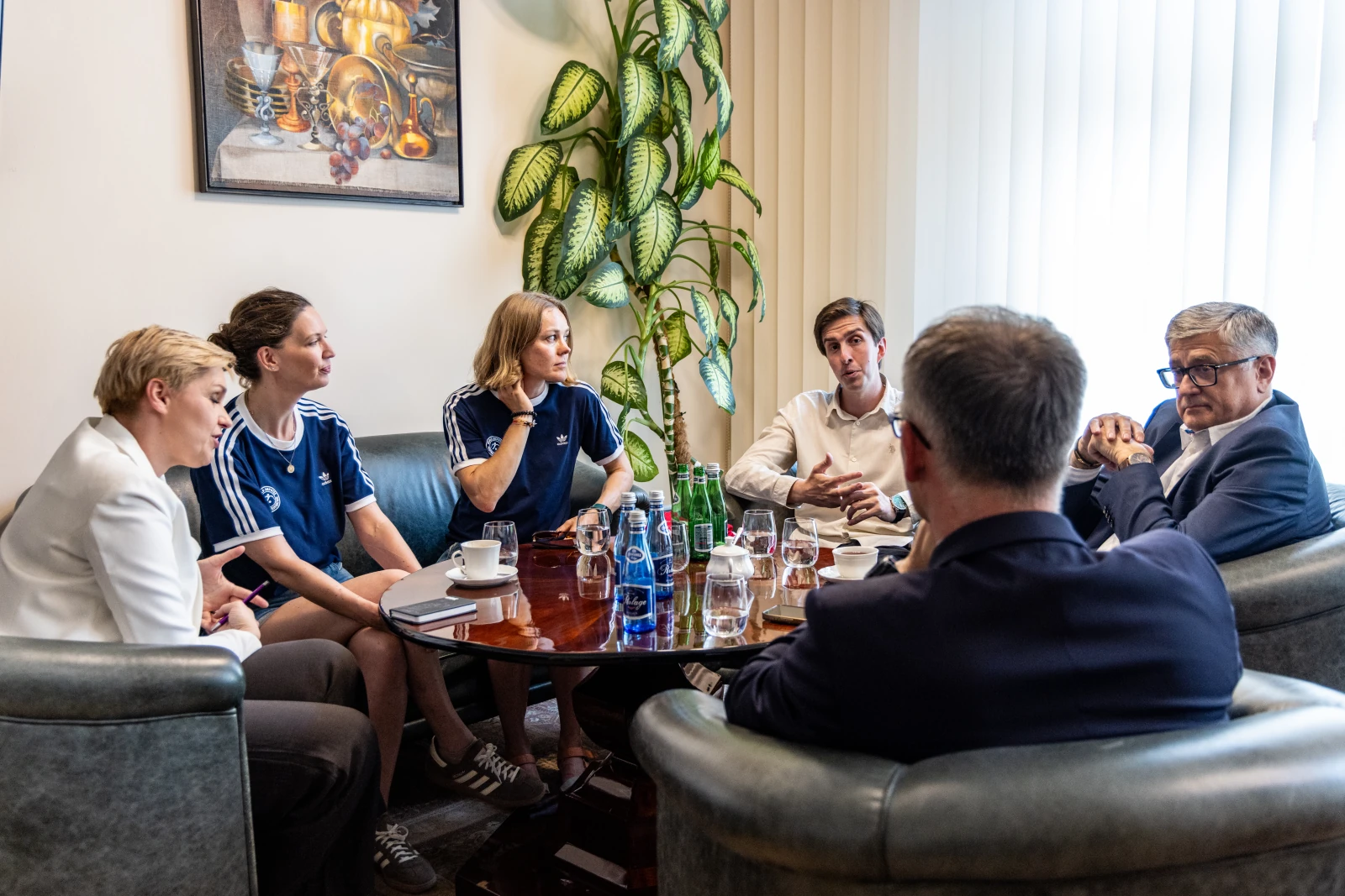 Grupa ludzi w dyskusji przy stole, w tle rośliny i napoje.  Autor: Jan Graczyński
