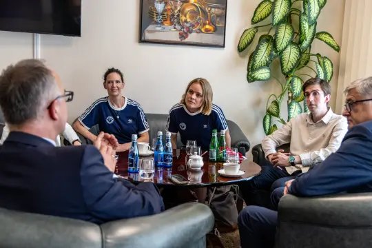 Spotkanie grupy osób w sportowych strojach, dyskutujących przy stole.