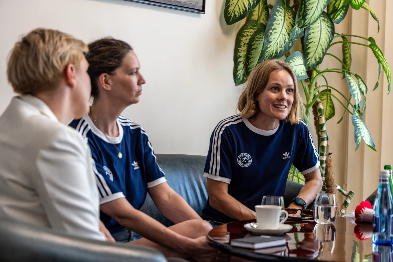 Trzy kobiety w sportowych koszulkach rozmawiają w przytulnym wnętrzu.  Autor: Jan Graczyński