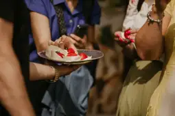 Osoby sięgające po deser z truskawkami na talerzu.