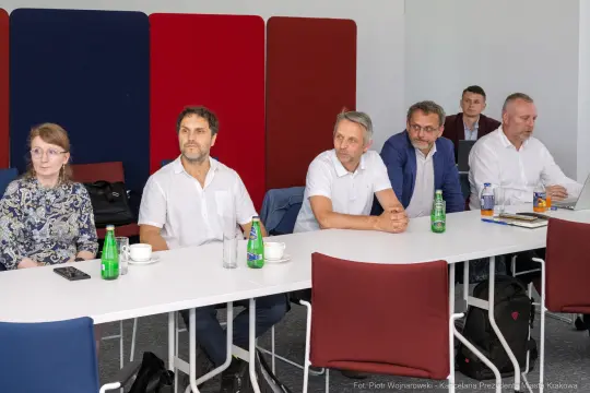 Grupa ludzi siedzących przy stole, uczestniczących w spotkaniu.
