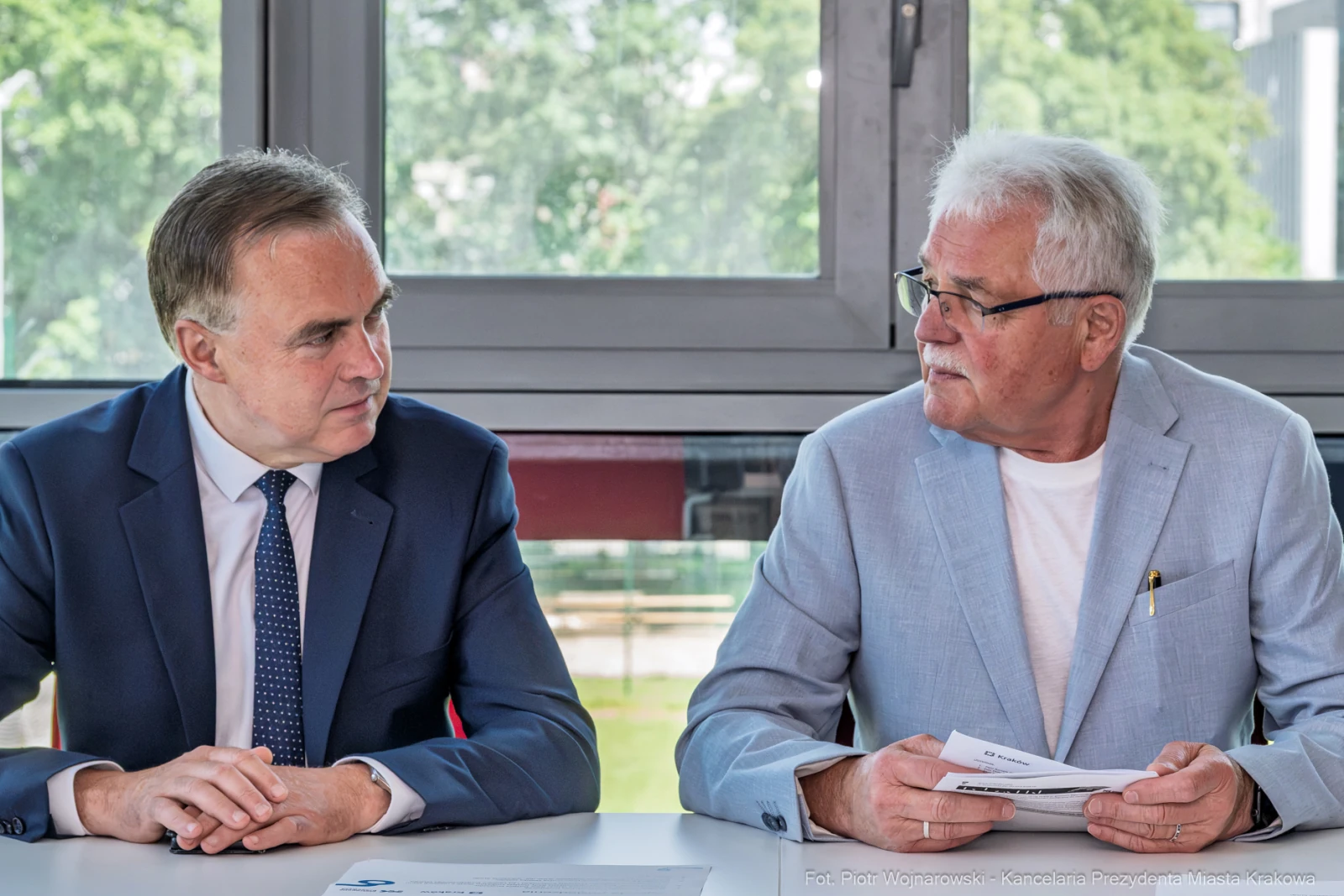 Dwaj mężczyźni siedzą przy stole, rozmawiając i trzymając dokumenty.  Autor: Piotr Wojnarowski