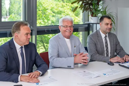 Trzech mężczyzn siedzących przy stole, uśmiechających się i rozmawiających.