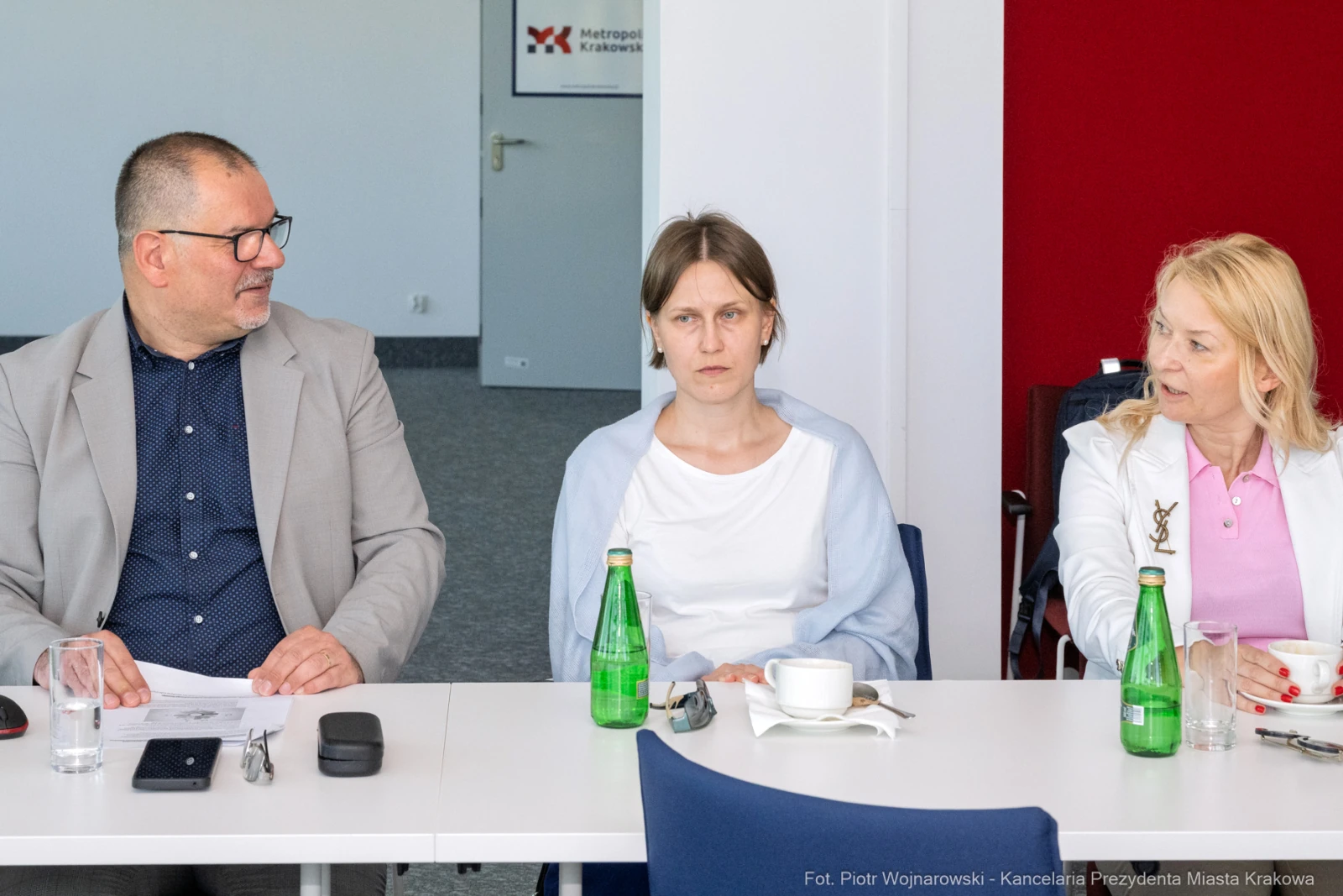 Trzy osoby siedzą przy stole, na stole butelki wody i filiżanka.  Autor: Piotr Wojnarowski