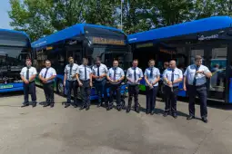 Grupa kierowców autobusów w uniformach stojąca obok pojazdów komunikacji miejskiej.