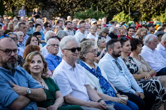 Tłum ludzi siedzących na wydarzeniu na świeżym powietrzu.
