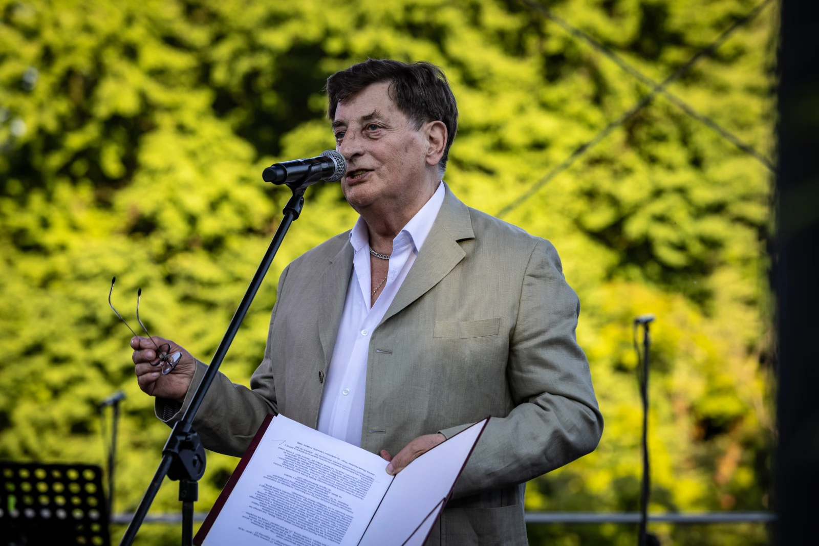 Mężczyzna w jasnym garniturze przemawia do mikrofonu, trzymając kartki z tekstem.  Autor: Bogusław Świerzowski