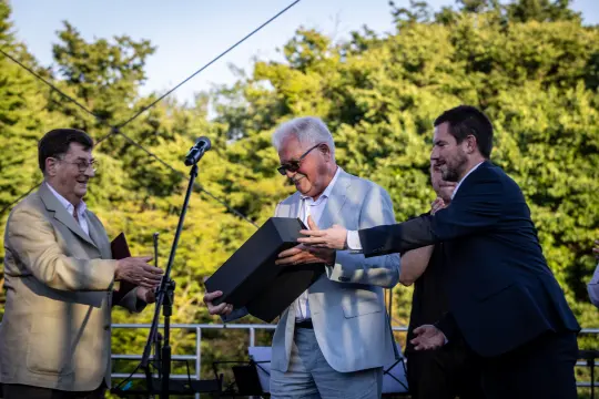Mężczyźni wręczają sobie nagrody na tle zieleni.
