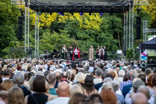 Występ artystyczny na scenie przed dużą publicznością w plenerze.
