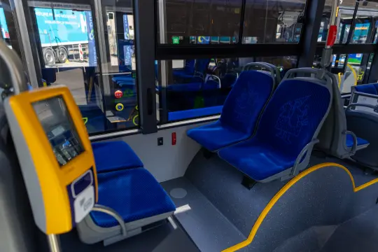 Wnętrze autobusu z niebieskimi siedzeniami i elektronicznym panelem informacyjnym.