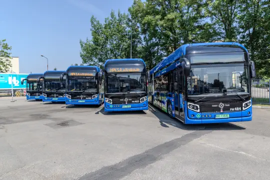 Cztery niebieskie autobusy stojące na parkingu w słoneczny dzień.