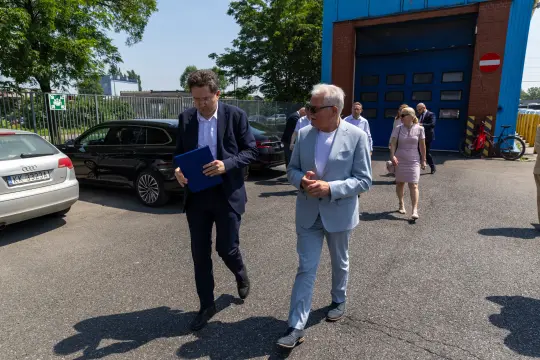 Dwaj mężczyźni rozmawiają na tle samochodów i budynku. Słoneczny dzień.