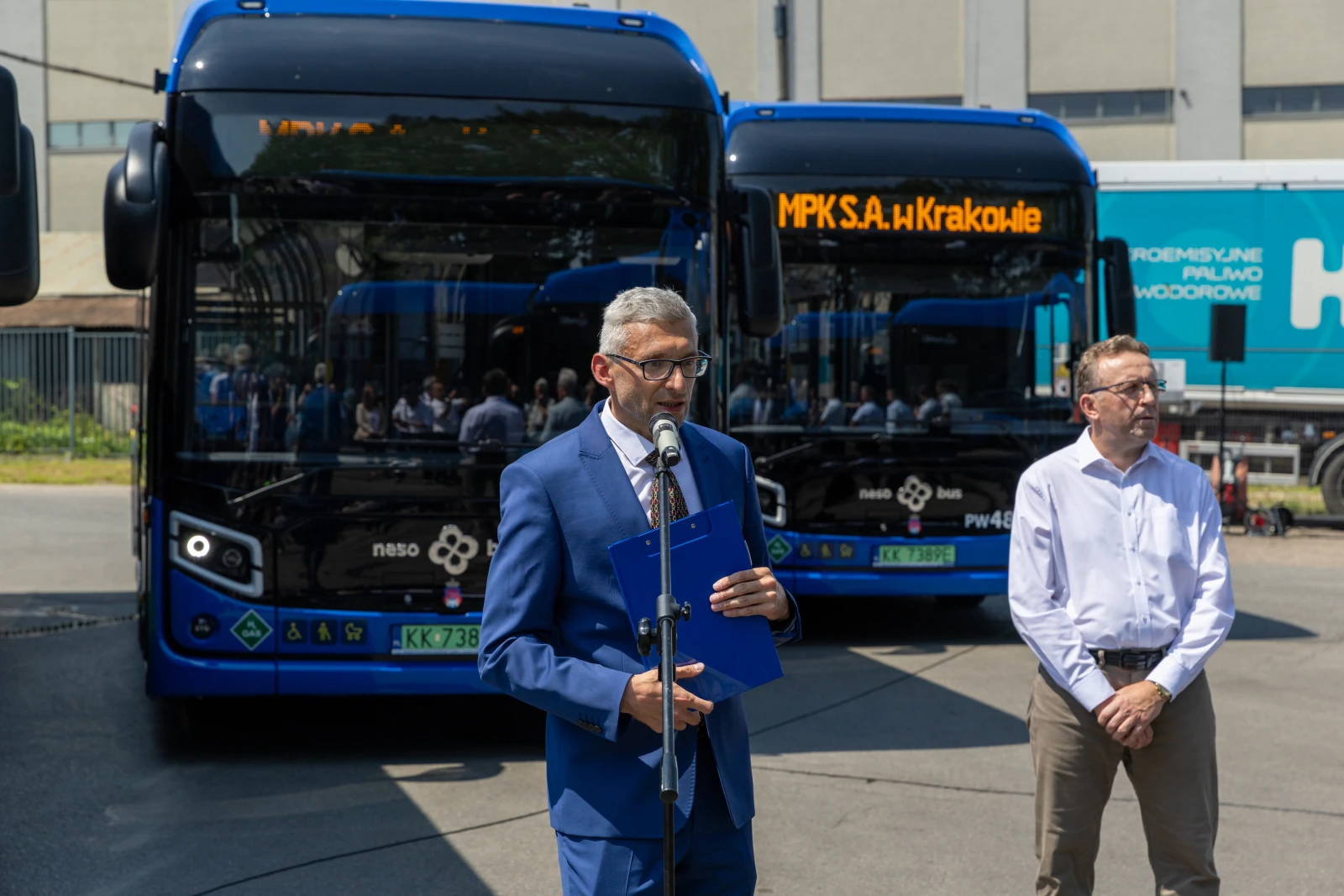 Mężczyzna w garniturze przemawia obok nowoczesnych autobusów MPK w Krakowie.  Autor: Bogusław Świerzowski