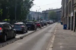 Ruch uliczny w mieście, samochody stoją w korku, widok na budynki i zieleń.