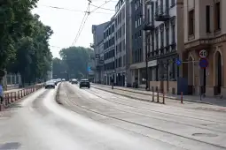 Ulica z torami tramwajowymi, samochodami i budynkami w tle.