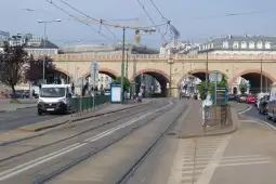 Ulica z torami tramwajowymi, mostem i ruchem samochodowym.