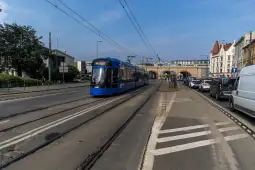 Niebieski tramwaj na ulicy, obok ruch samochodowy i architektura miejska.
