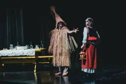 Dwóch aktorów w strojach ludowych na scenie, jeden w kostiumie ze słomy, drugi z lampionem.