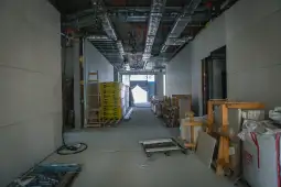 Korytarz budowlany z materiałami i narzędziami, w tle widoczna jasna przestrzeń.