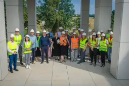 Grupa ludzi w kamizelkach odblaskowych i kaskach budowlanych na placu budowy.
