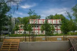 Nowoczesny budynek w trakcie budowy otoczony drzewami i zielenią.